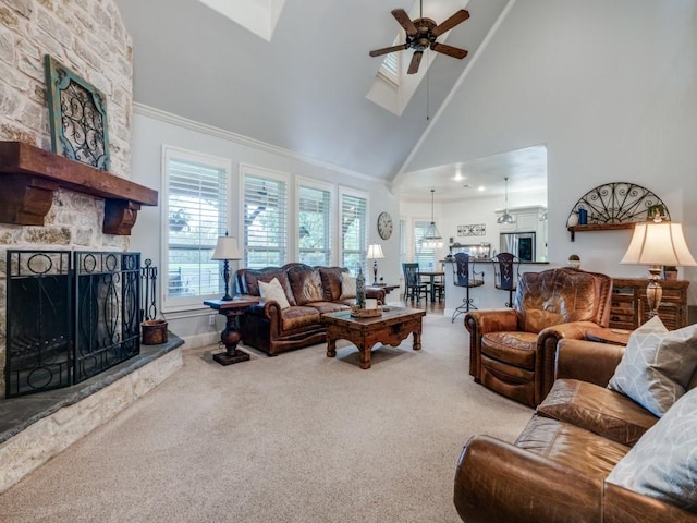 living room featuring a skylight, a ceiling fan, carpet flooring, a stone fireplace, and high vaulted ceiling