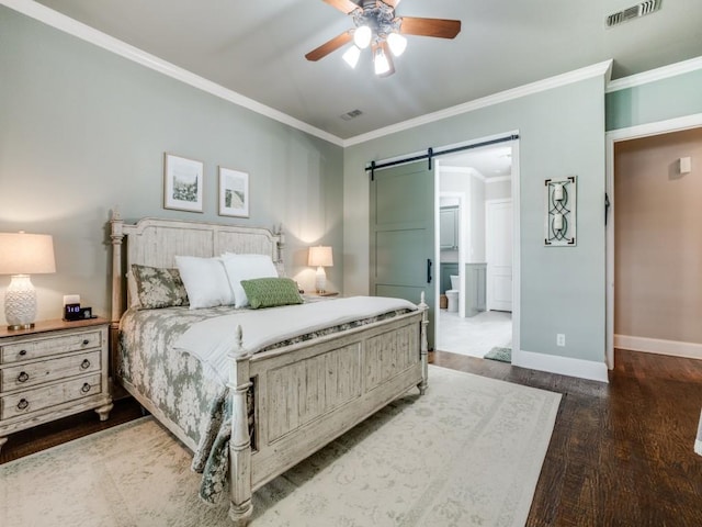 bedroom with wood finished floors, visible vents, crown molding, and a barn door