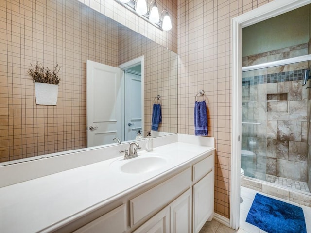 bathroom featuring tile patterned flooring, toilet, vanity, tile walls, and a shower stall