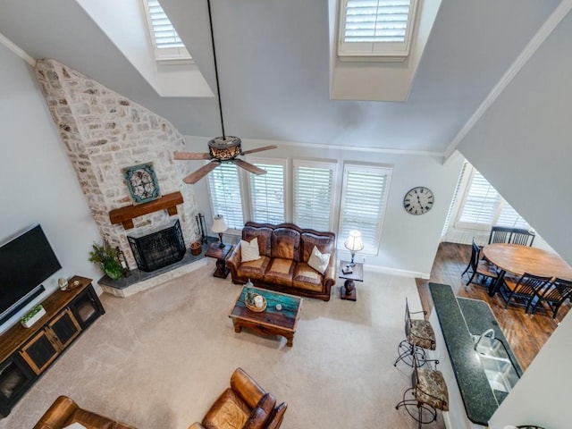 carpeted living area with ceiling fan, a fireplace, baseboards, and crown molding