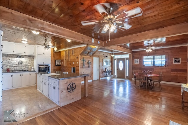 kitchen with ceiling fan, beamed ceiling, dark countertops, and light wood-style floors