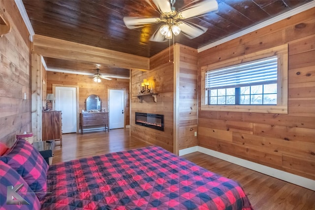 bedroom featuring wooden walls, baseboards, a glass covered fireplace, wood ceiling, and wood finished floors