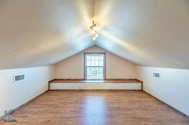 bonus room with a textured ceiling, wood finished floors, and visible vents