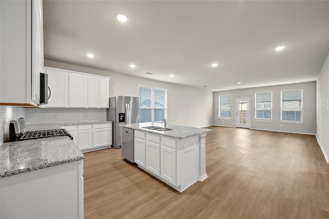 kitchen featuring light wood finished floors, tasteful backsplash, appliances with stainless steel finishes, a sink, and light stone countertops