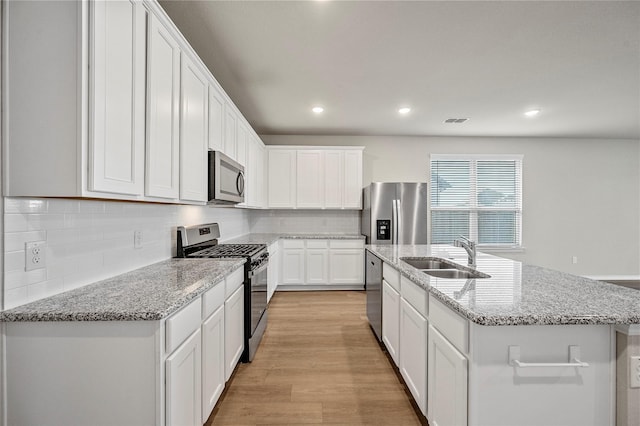 kitchen featuring stainless steel appliances, light wood-style floors, white cabinets, a kitchen island with sink, and a sink