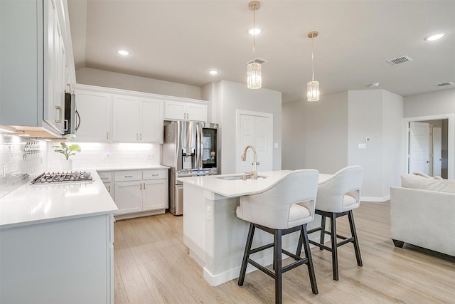 kitchen featuring light wood finished floors, tasteful backsplash, visible vents, appliances with stainless steel finishes, and a sink