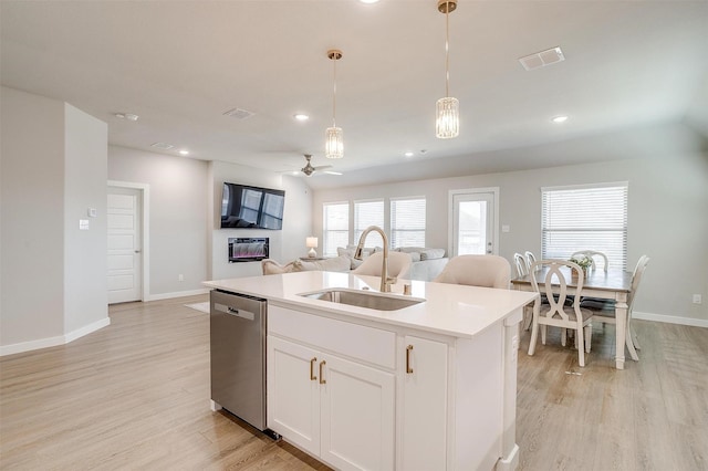 kitchen with a kitchen island with sink, a sink, hanging light fixtures, stainless steel dishwasher, and light wood finished floors