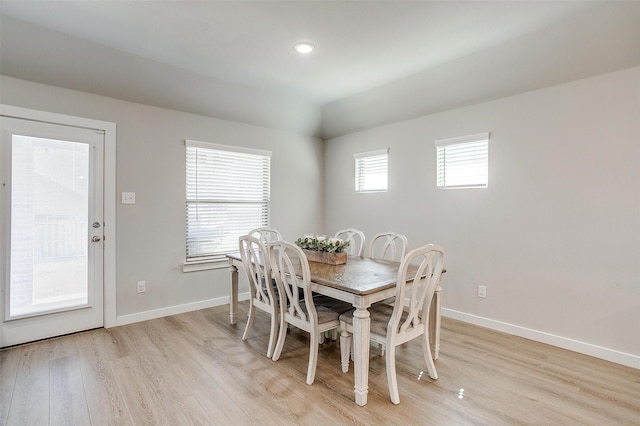 dining room with light wood-type flooring, vaulted ceiling, and baseboards