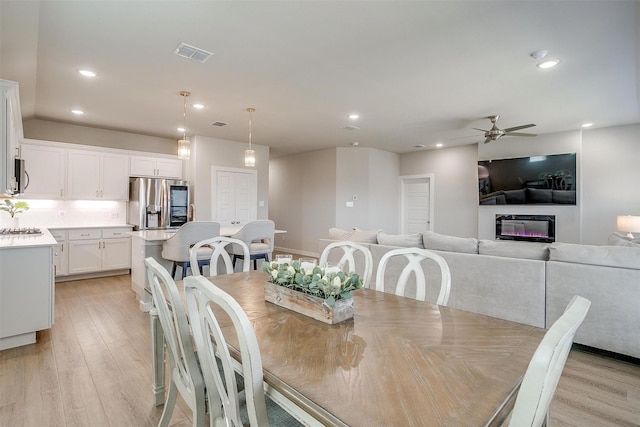 dining room featuring light wood finished floors, a glass covered fireplace, visible vents, and recessed lighting