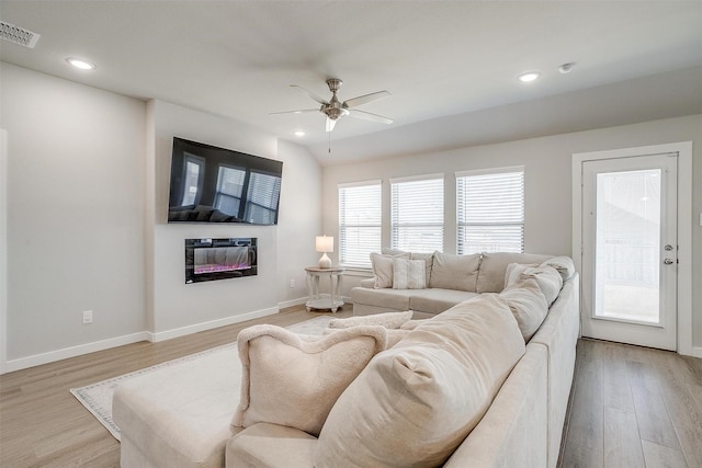 living area with light wood-style floors, baseboards, visible vents, and a glass covered fireplace