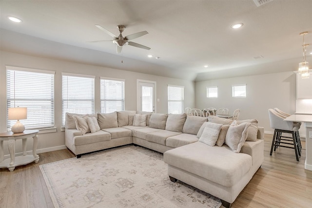 living room with light wood-style flooring, ceiling fan with notable chandelier, baseboards, and recessed lighting