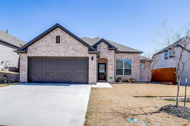 french country style house featuring a garage, brick siding, driveway, and a shingled roof