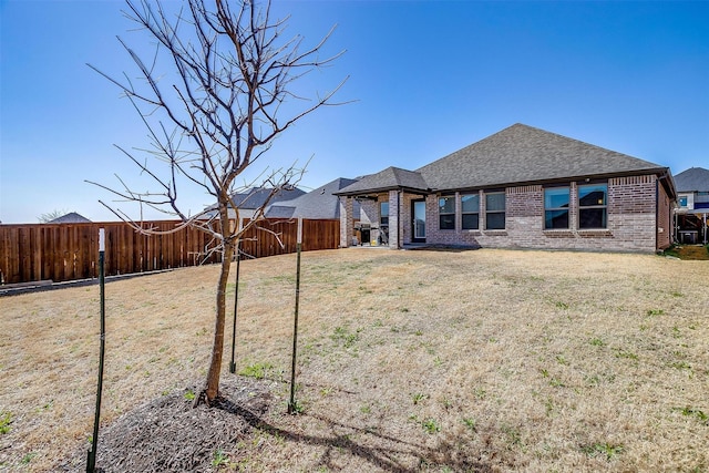 back of property with roof with shingles, brick siding, a lawn, and a fenced backyard