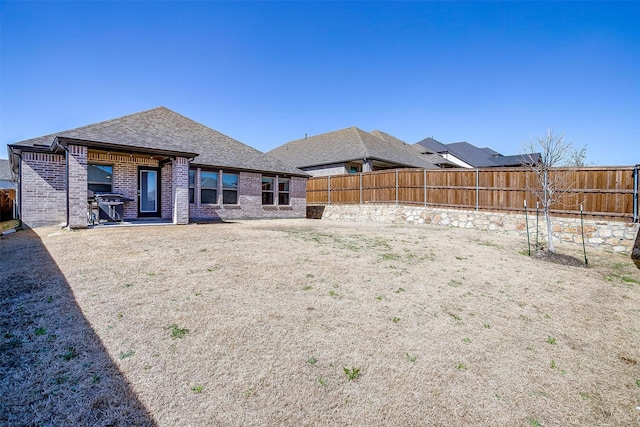 back of house with brick siding, a shingled roof, and a fenced backyard