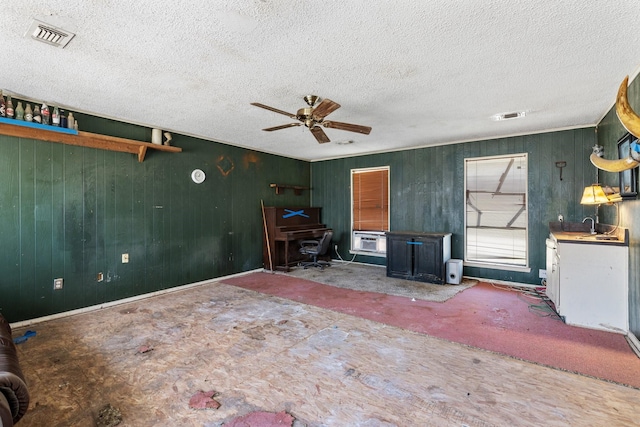 unfurnished living room with ceiling fan, a textured ceiling, visible vents, and baseboards