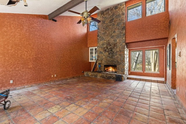 unfurnished living room with a towering ceiling, ceiling fan, beam ceiling, and a stone fireplace