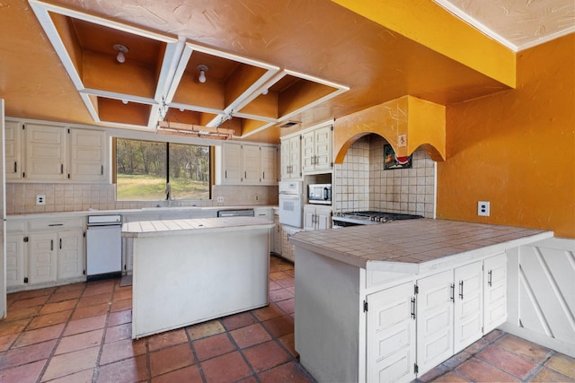 kitchen featuring tile countertops, white oven, stainless steel microwave, and decorative backsplash