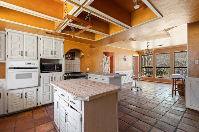 kitchen with tile counters, white cabinets, appliances with stainless steel finishes, a peninsula, and a chandelier