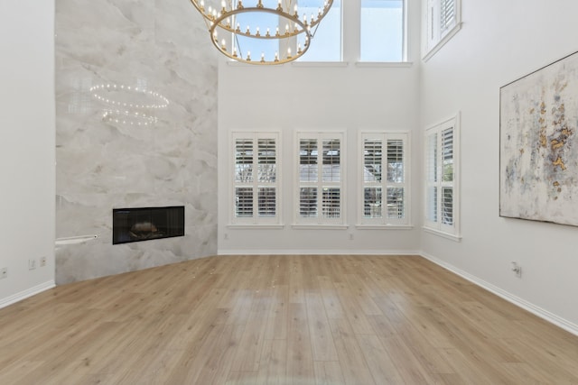 unfurnished living room with a fireplace, a high ceiling, an inviting chandelier, wood finished floors, and baseboards