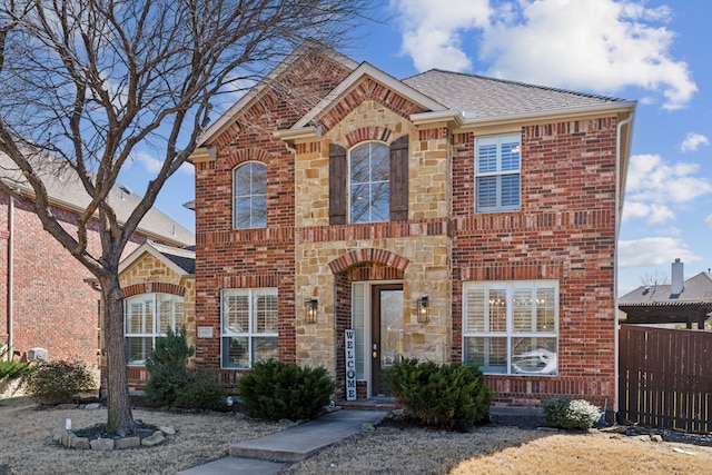 view of front of house with stone siding, brick siding, roof with shingles, and fence