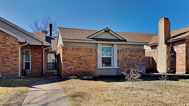 view of front facade with roof with shingles, a front yard, and brick siding