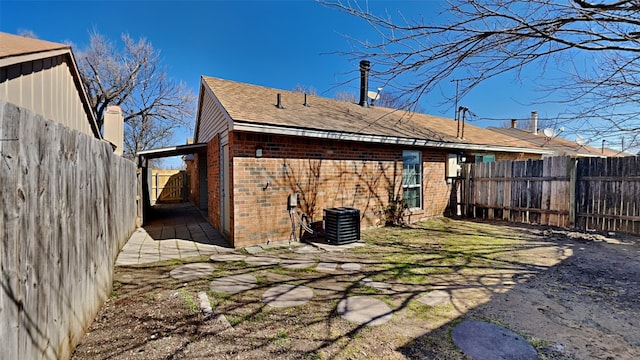 rear view of property with brick siding, roof with shingles, central AC unit, and a fenced backyard