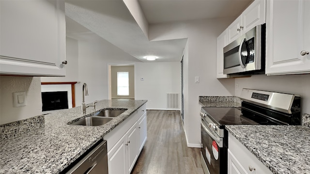 kitchen featuring stainless steel appliances, light stone countertops, a sink, and wood finished floors