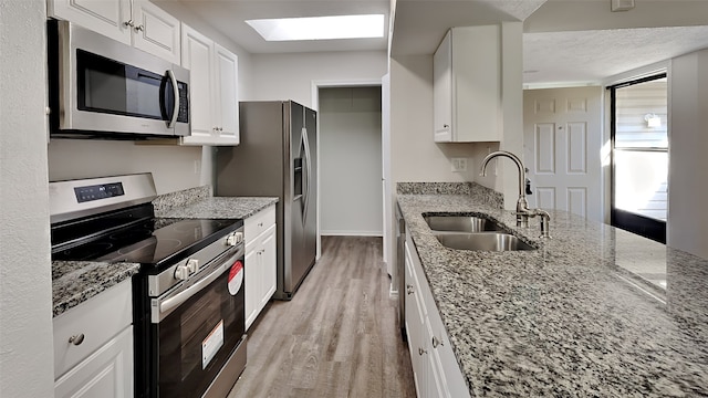 kitchen with white cabinets, light stone counters, stainless steel appliances, light wood-style floors, and a sink