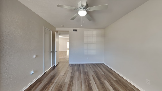 spare room with visible vents, a textured wall, a ceiling fan, wood finished floors, and baseboards