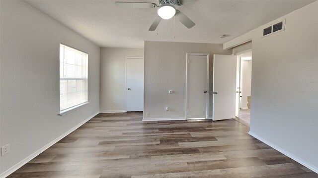 unfurnished bedroom with a ceiling fan, wood finished floors, visible vents, and baseboards