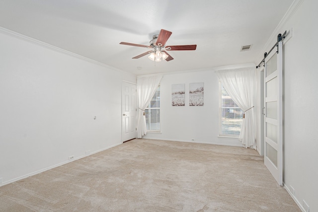 empty room with light carpet, a barn door, visible vents, ceiling fan, and ornamental molding