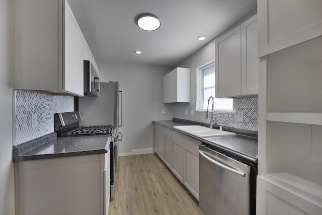 kitchen featuring stainless steel appliances, a sink, light wood-type flooring, tasteful backsplash, and dark countertops