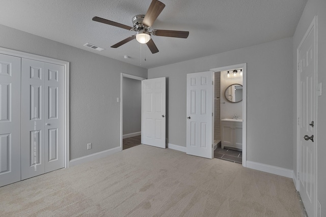 unfurnished bedroom with a textured ceiling, connected bathroom, visible vents, a closet, and carpet