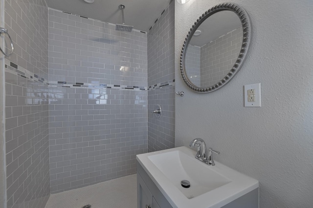 full bath featuring tiled shower, a textured wall, and vanity