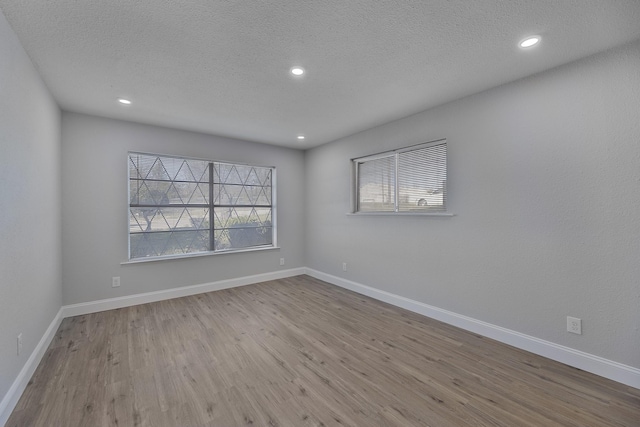 spare room with a textured ceiling, recessed lighting, wood finished floors, and baseboards