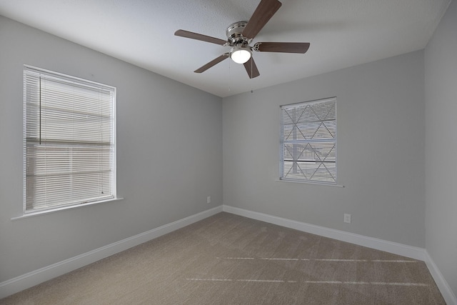 empty room with a ceiling fan, dark colored carpet, and baseboards