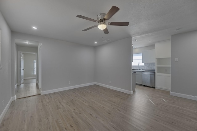 unfurnished living room featuring visible vents, a sink, light wood-style flooring, and baseboards