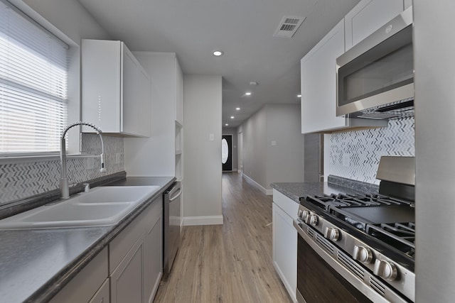 kitchen featuring stainless steel appliances, visible vents, a sink, light wood-type flooring, and baseboards