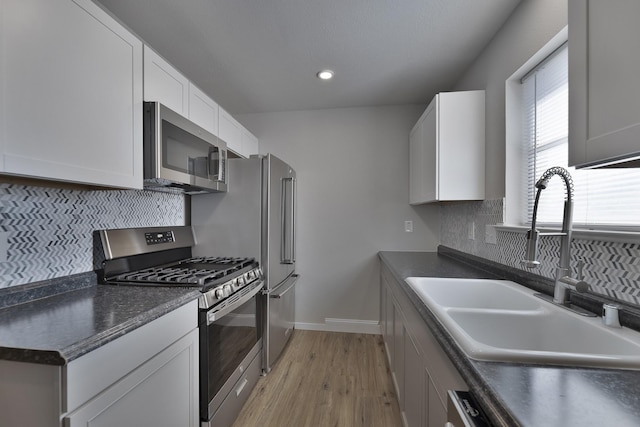 kitchen featuring stainless steel appliances, dark countertops, backsplash, white cabinetry, and a sink