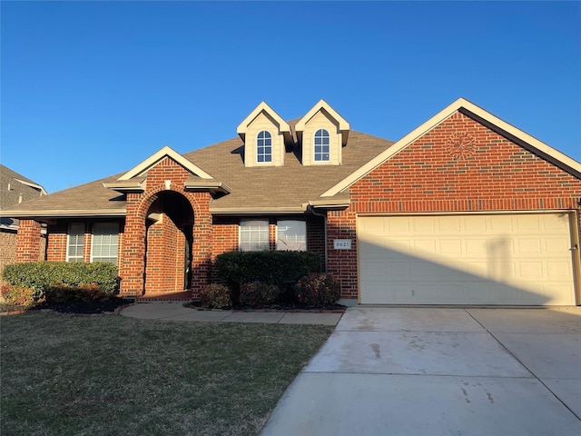 view of front of home featuring an attached garage, brick siding, concrete driveway, roof with shingles, and a front yard