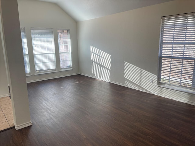 empty room with dark wood-type flooring, vaulted ceiling, and baseboards