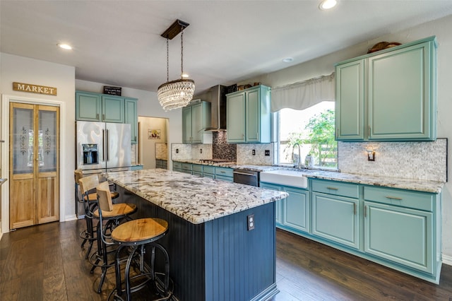 kitchen featuring dark wood finished floors, wall chimney exhaust hood, a center island, stainless steel appliances, and a sink