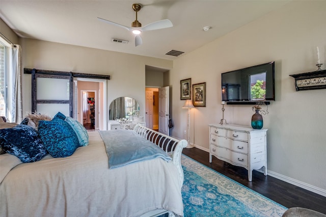 bedroom with a walk in closet, wood finished floors, visible vents, and baseboards