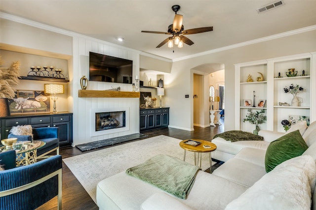 living room with a large fireplace, visible vents, arched walkways, dark wood finished floors, and crown molding