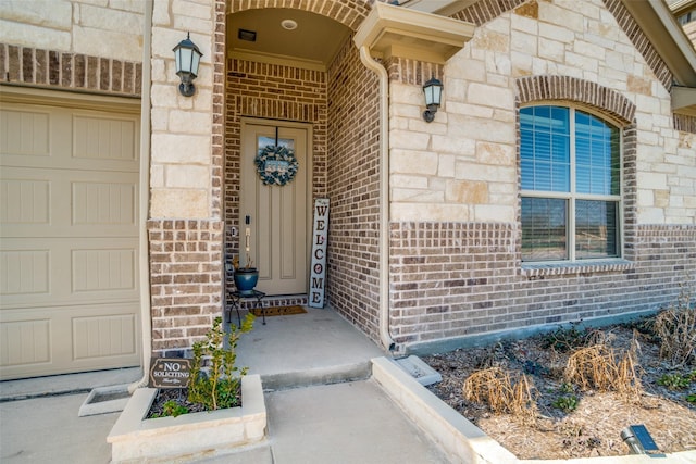 view of exterior entry featuring stone siding, brick siding, and an attached garage