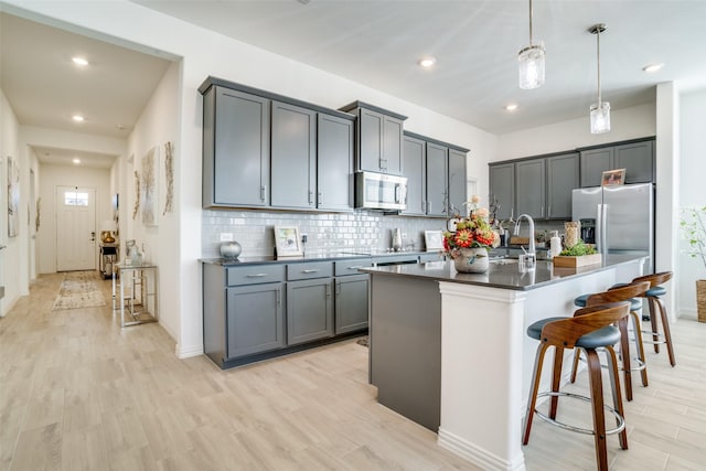 kitchen featuring tasteful backsplash, dark countertops, appliances with stainless steel finishes, light wood-type flooring, and a kitchen breakfast bar