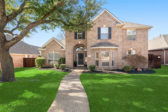 traditional home with brick siding, roof with shingles, a front yard, and fence