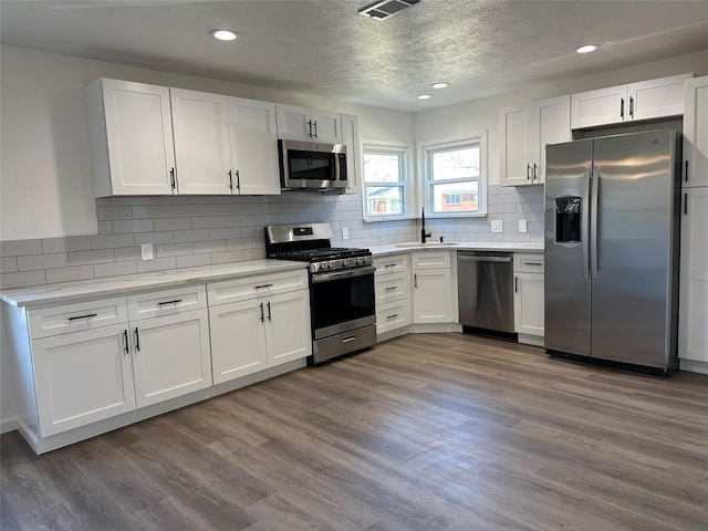 kitchen with dark wood-style flooring, stainless steel appliances, light countertops, white cabinetry, and a sink