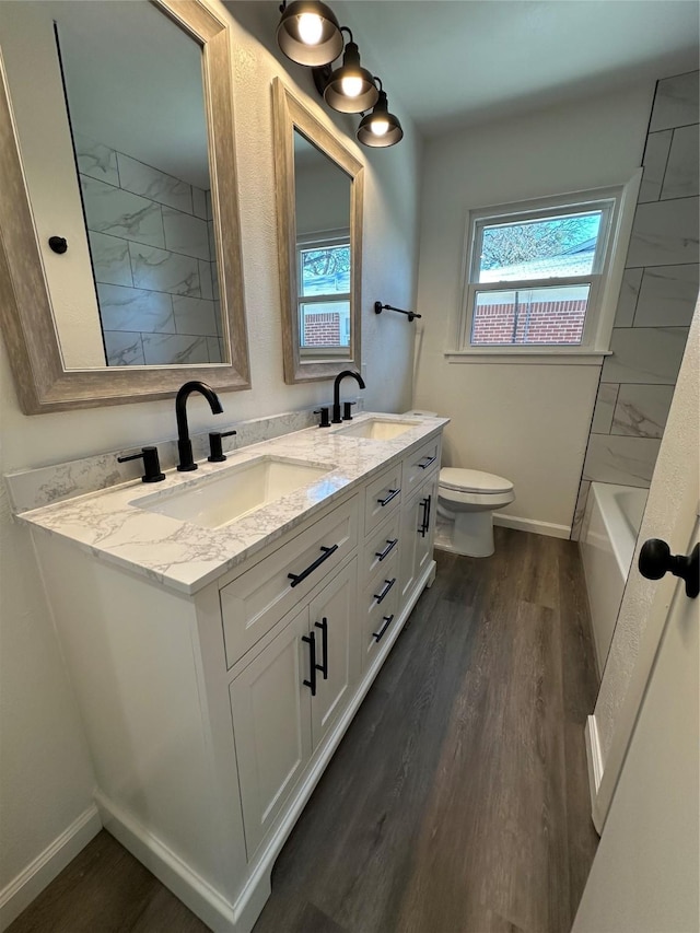 full bath with toilet, baseboards, a sink, and wood finished floors