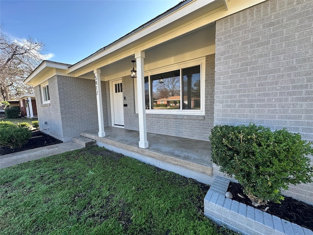 entrance to property with covered porch, brick siding, and a yard